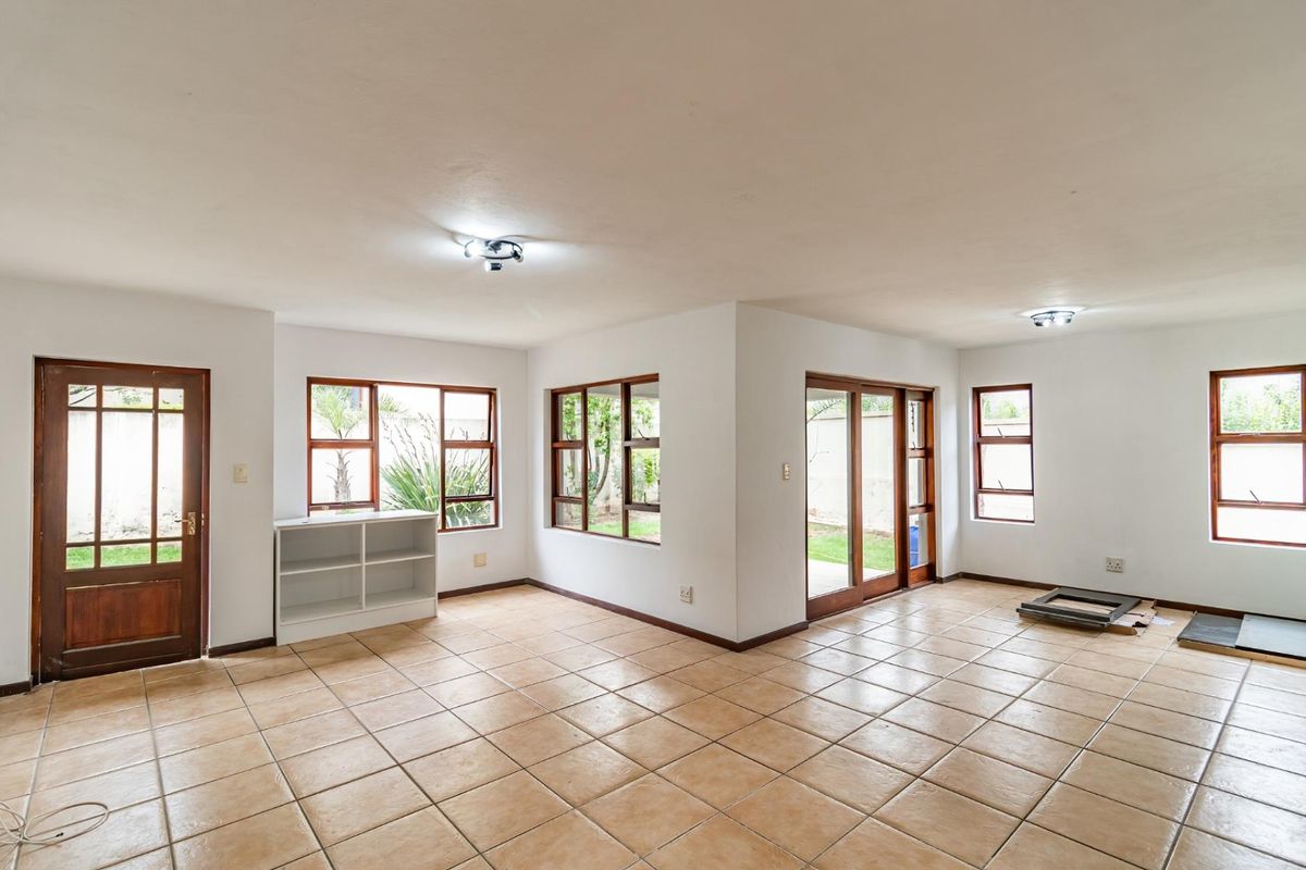 Spacious, light-filled living area featuring neutral tiled flooring, large wooden-framed windows, and sliding glass doors providing direct access to the garden.