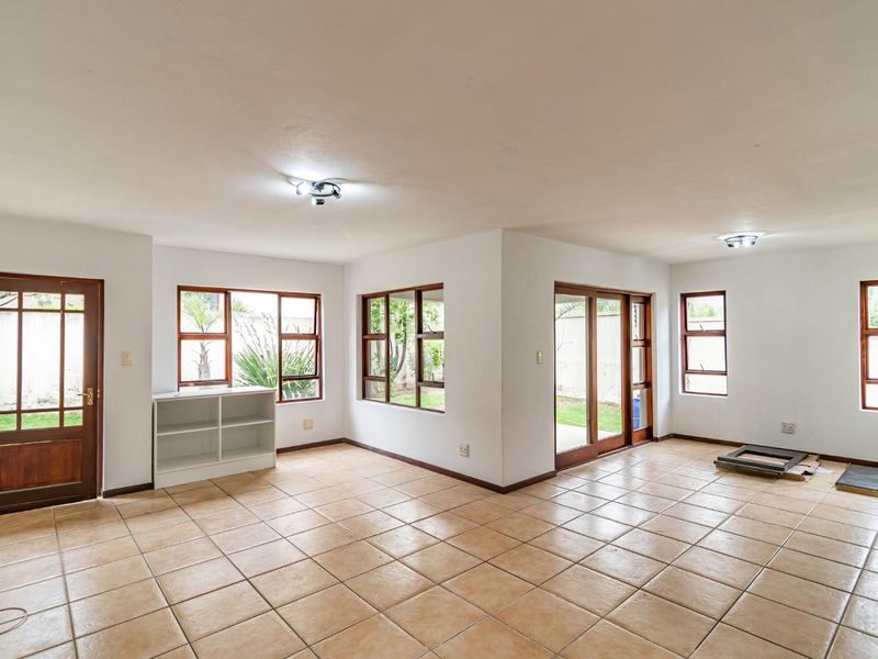 Spacious, light-filled living area featuring neutral tiled flooring, large wooden-framed windows, and sliding glass doors providing direct access to the garden.