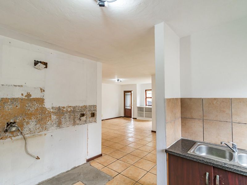 An open-plan kitchen area in need of renovation, featuring tiled flooring, a stainless steel sink, and exposed wall sections requiring repair.