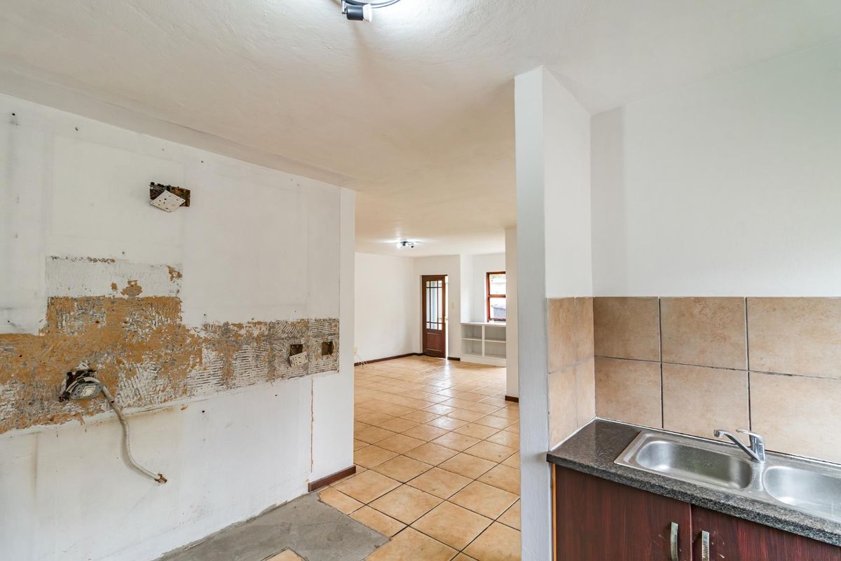 An open-plan kitchen area in need of renovation, featuring tiled flooring, a stainless steel sink, and exposed wall sections requiring repair.