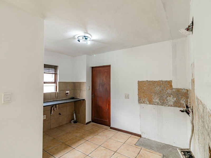A vacant kitchen space requiring renovation, featuring tiled flooring, a stone countertop, and exposed wall areas ready for finishing or cabinetry installation.