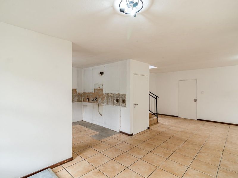 An empty open-plan living area featuring ceramic floor tiles, a staircase, and a wall area requiring renovation and repair of plaster and electrical fixtures.