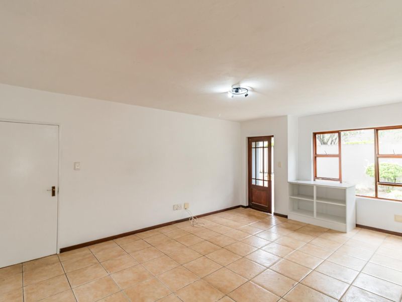 A bright, empty living area featuring neutral tiled flooring, a timber-framed entrance door, and a built-in shelving unit under the window.