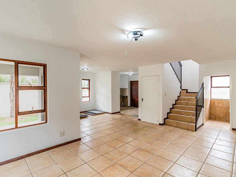 Spacious open-plan living area featuring tiled flooring, a central staircase with metal balustrades, and direct access to kitchen and utility spaces.