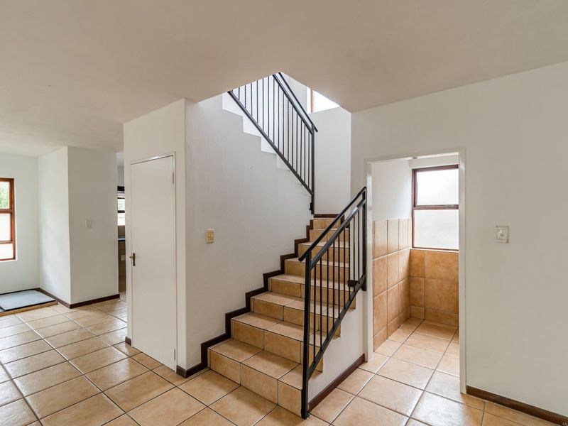 A bright, tiled hallway featuring a central staircase with a metal balustrade, leading to upper levels with neutral wall finishes.