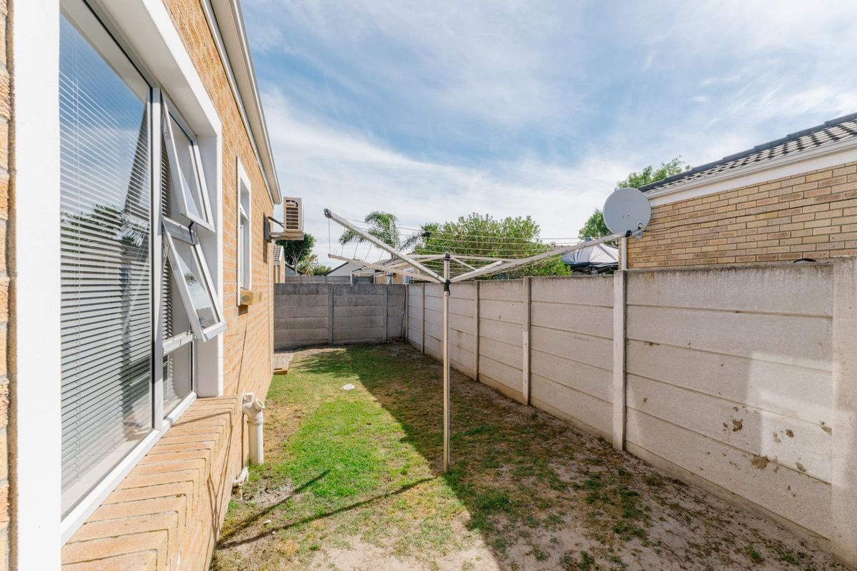 A rear exterior view of the townhouse featuring a small lawn area, precast concrete boundary wall, and a rotary clothesline.