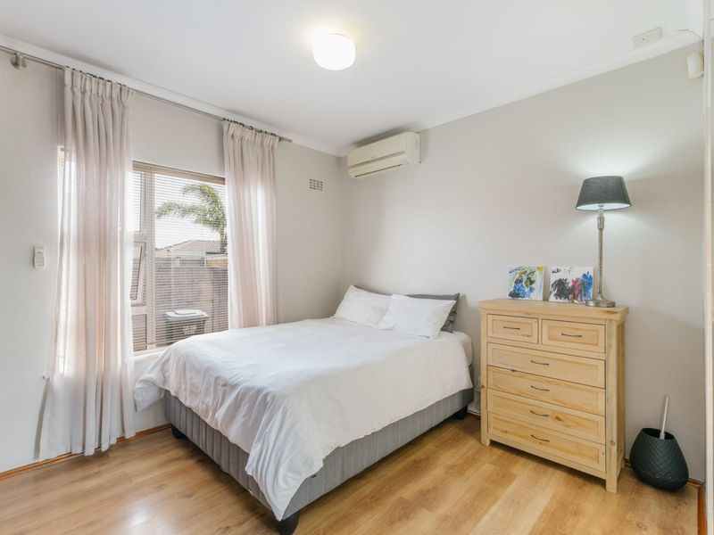 A well-maintained bedroom featuring laminate flooring, a wall-mounted split-system air conditioner, and large windows allowing for natural light.