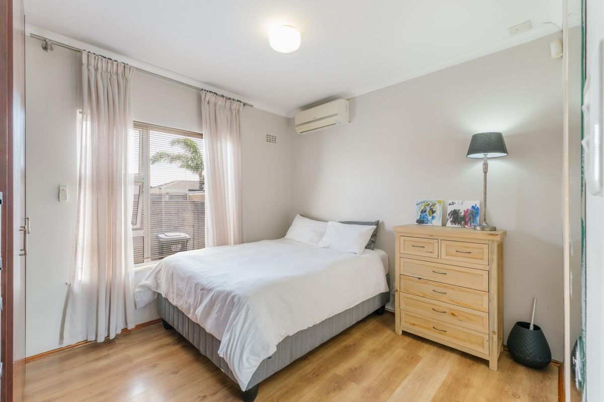 A well-maintained bedroom featuring laminate flooring, a wall-mounted split-system air conditioner, and large windows allowing for natural light.