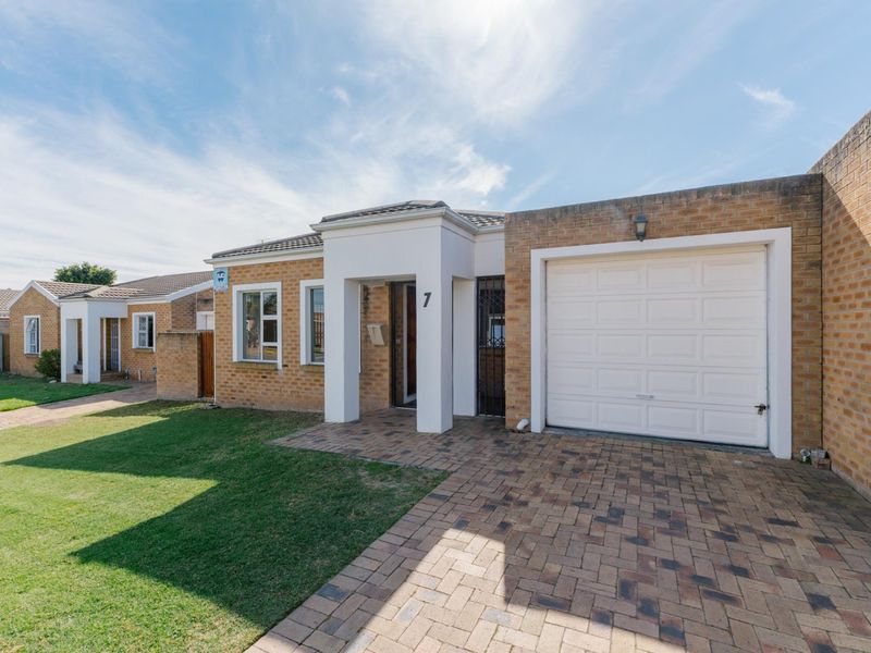 Front elevation of a single-story townhouse featuring a brick facade, paved driveway, single garage, and a well-maintained front lawn.