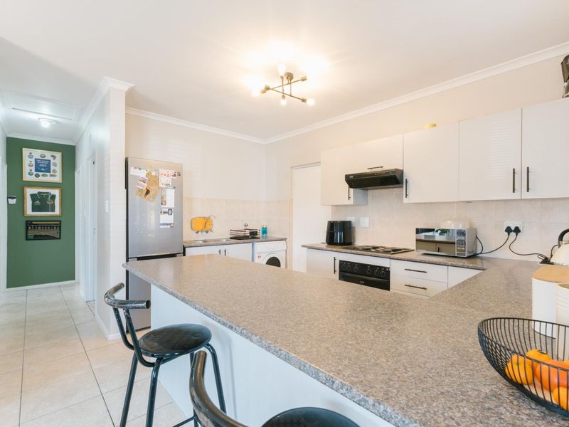 Modern kitchen featuring white cabinetry, laminate countertops, a breakfast bar, and integrated appliances, with tiled flooring and a neutral color palette.
