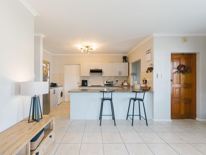 Open plan living area featuring a functional kitchen with granite countertops, breakfast bar, and tiled flooring throughout, leading to a traditional timber entrance door.