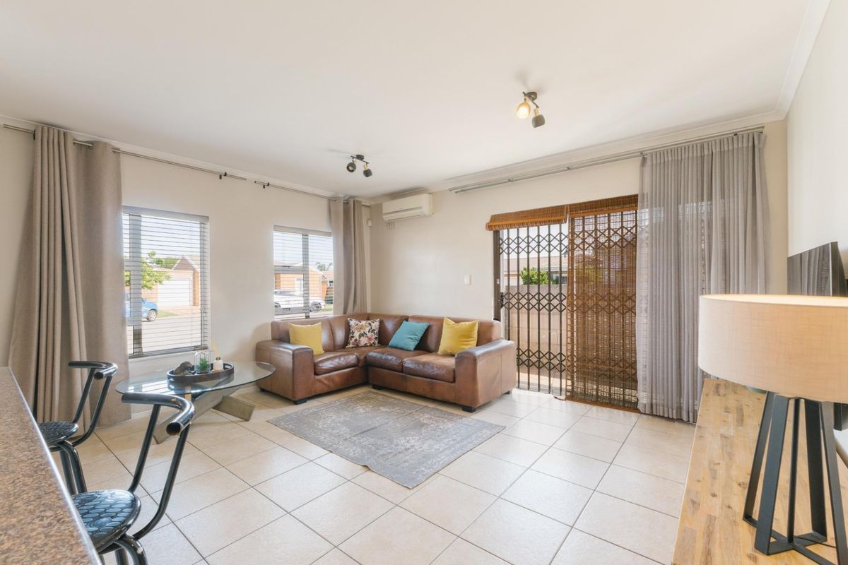 Bright living room featuring tiled flooring, a wall-mounted air conditioning unit, and sliding glass doors with security gate access to the exterior.