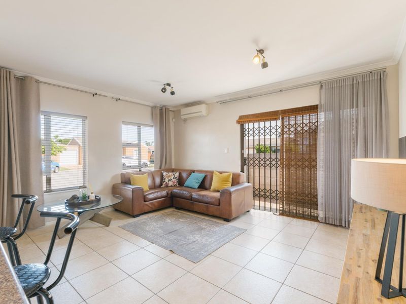 Bright living room featuring tiled flooring, a wall-mounted air conditioning unit, and sliding glass doors with security gate access to the exterior.