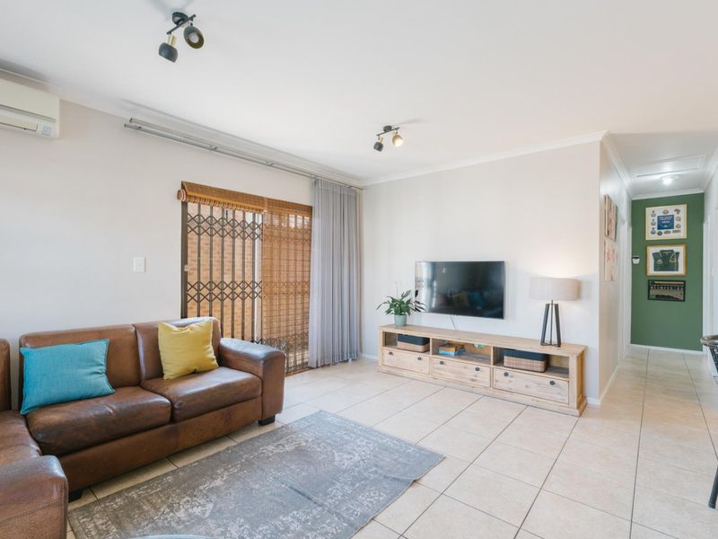 A bright and well-maintained living room featuring tiled flooring, a split-system air conditioner, and a sliding glass door with security gate access.