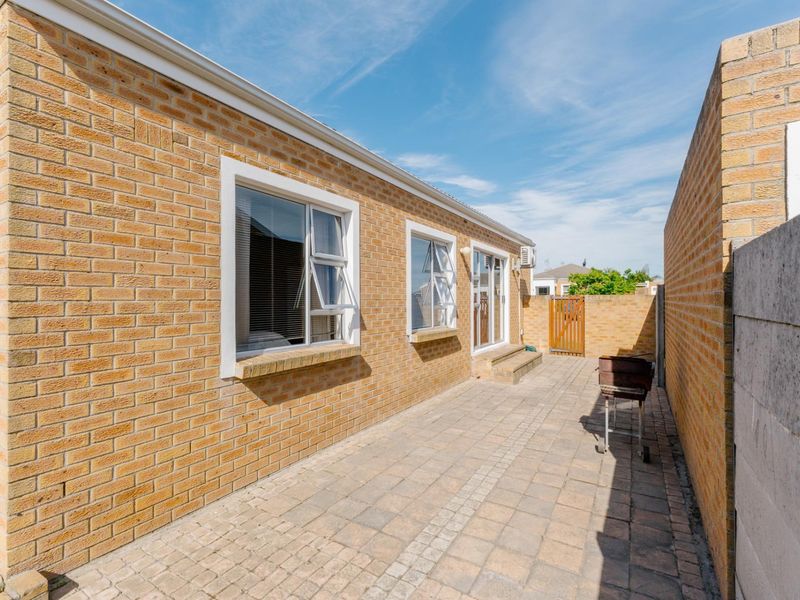 A private rear courtyard featuring a paved patio area, face brick exterior walls, and secure boundary walling with a wooden access gate.