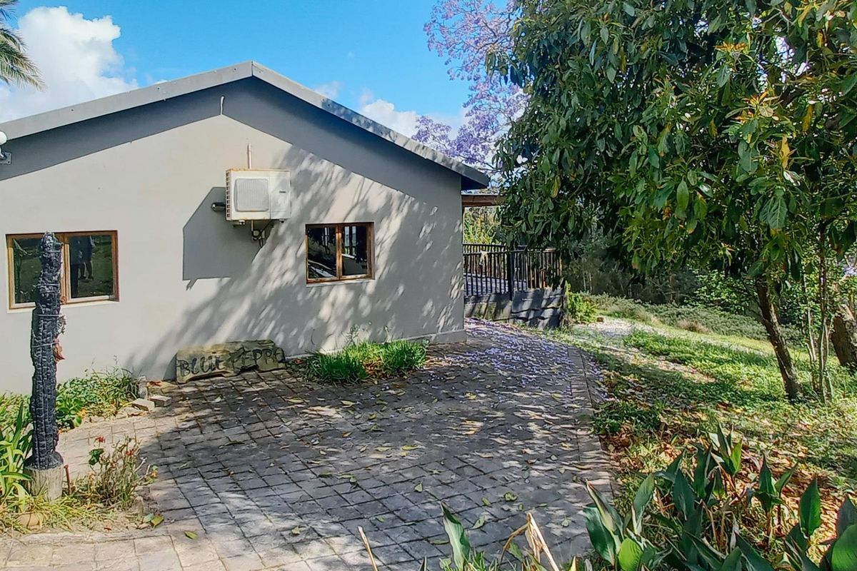 Rear view of the property featuring a paved walkway, timber deck, and exterior air conditioning unit set within a landscaped garden.
