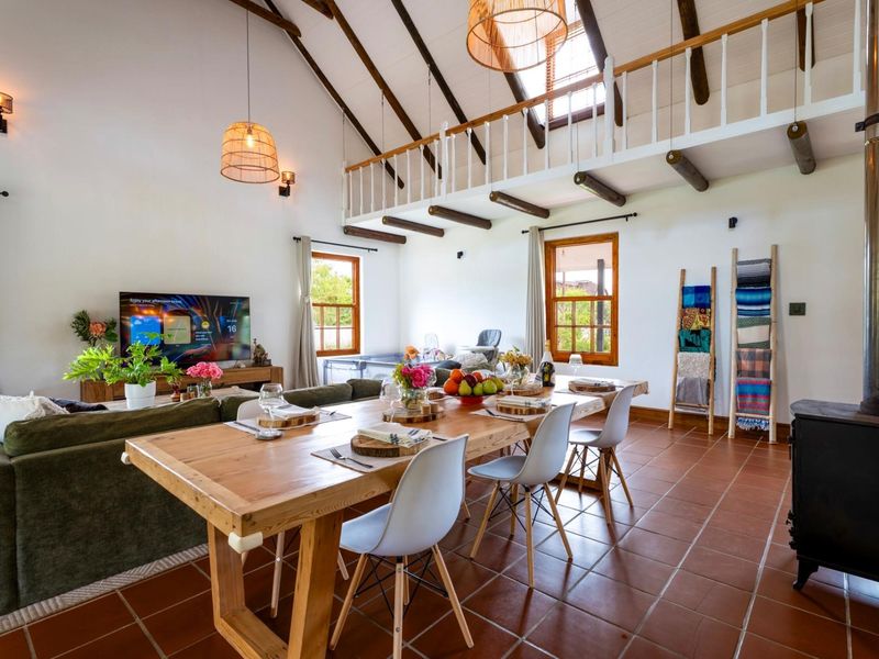 Spacious open-plan living and dining area featuring a high vaulted ceiling with exposed timber beams, a mezzanine level, and a cozy wood-burning stove.