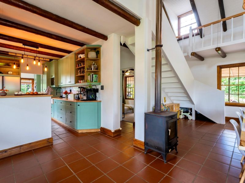 Open-plan living area featuring a modern kitchen with green cabinetry, exposed timber beams, a wood-burning fireplace, and a staircase leading to a mezzanine level.