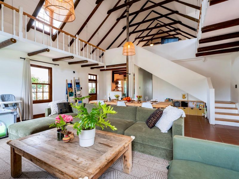 Spacious open-plan living and dining area featuring high vaulted ceilings with exposed timber trusses, a mezzanine level, and classic terracotta flooring.