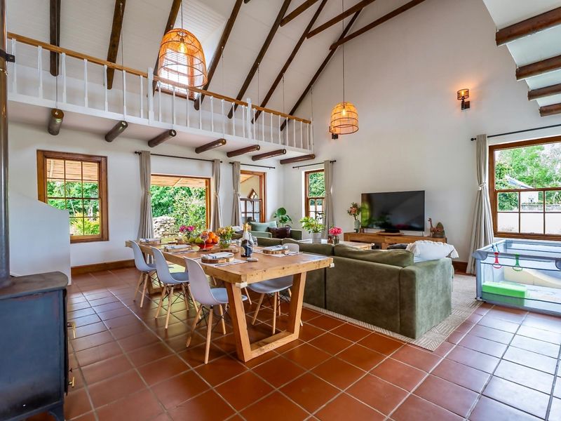 Spacious open-plan living and dining area featuring a dramatic vaulted ceiling with exposed timber beams, a mezzanine level, and a cozy wood-burning stove.