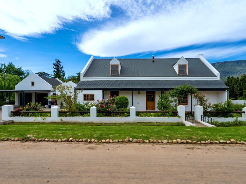 Charming Cape Dutch style house featuring a corrugated metal roof, dormer windows, a covered veranda, and a well-maintained front garden with a detached garage.