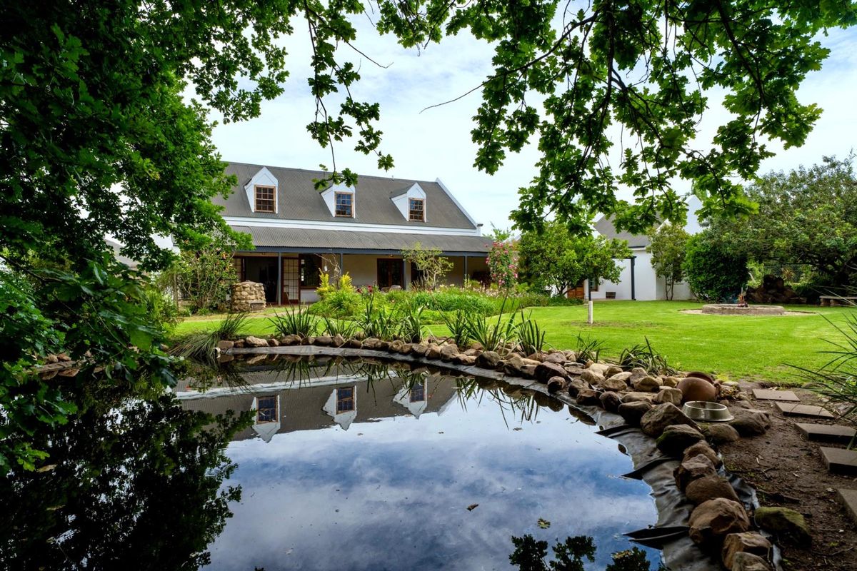 A picturesque rear view of the house featuring a landscaped garden, a stone-lined pond, and a covered patio area.