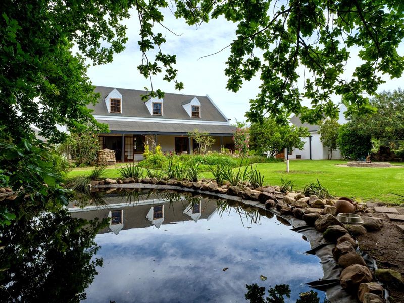 A picturesque rear view of the house featuring a landscaped garden, a stone-lined pond, and a covered patio area.