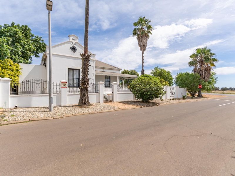 A well-maintained historic property featuring a classic gabled facade, secure wrought iron fencing, and a paved street-front entrance.