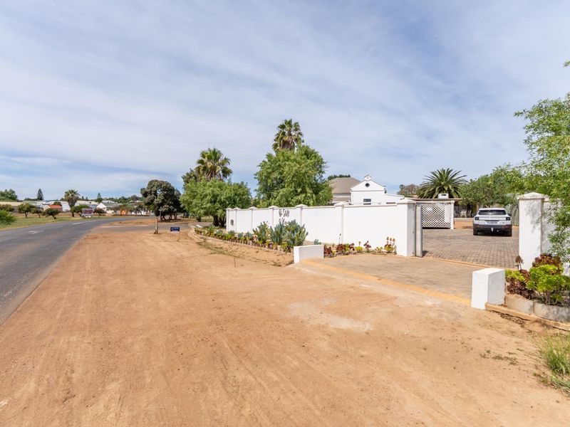Street view of the property entrance featuring a paved driveway, boundary wall, and established garden beds.