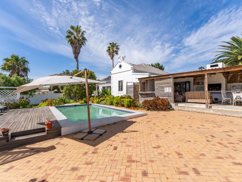 Outdoor entertainment area featuring a swimming pool, timber decking, brick-paved patio, and a covered pergola with a built-in braai.