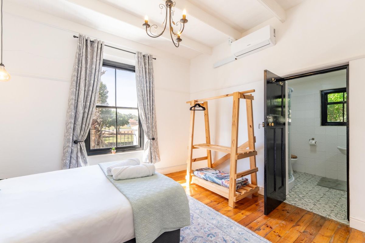 A bright bedroom featuring polished hardwood floors, exposed ceiling beams, a split-system air conditioner, and an adjoining en-suite bathroom.