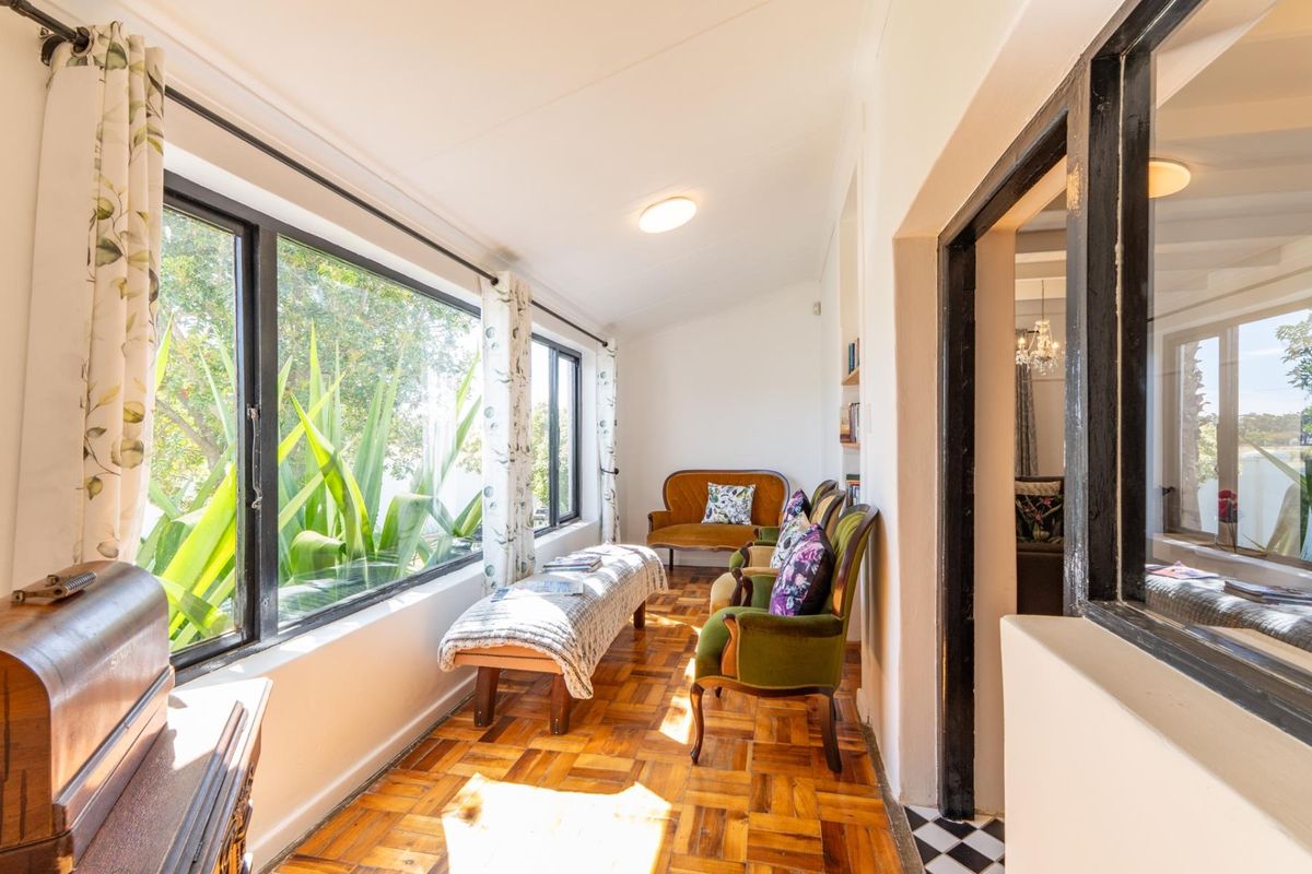 A sunlit sunroom or living area featuring classic parquet flooring, large windows with garden views, and built-in shelving.