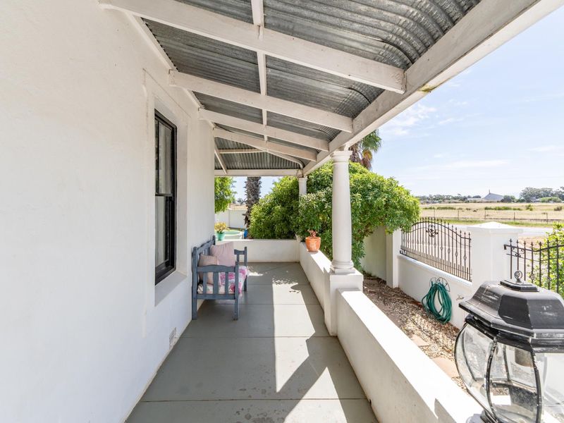 A covered veranda featuring a corrugated iron roof, classic support columns, and a masonry balustrade overlooking the surrounding landscape.