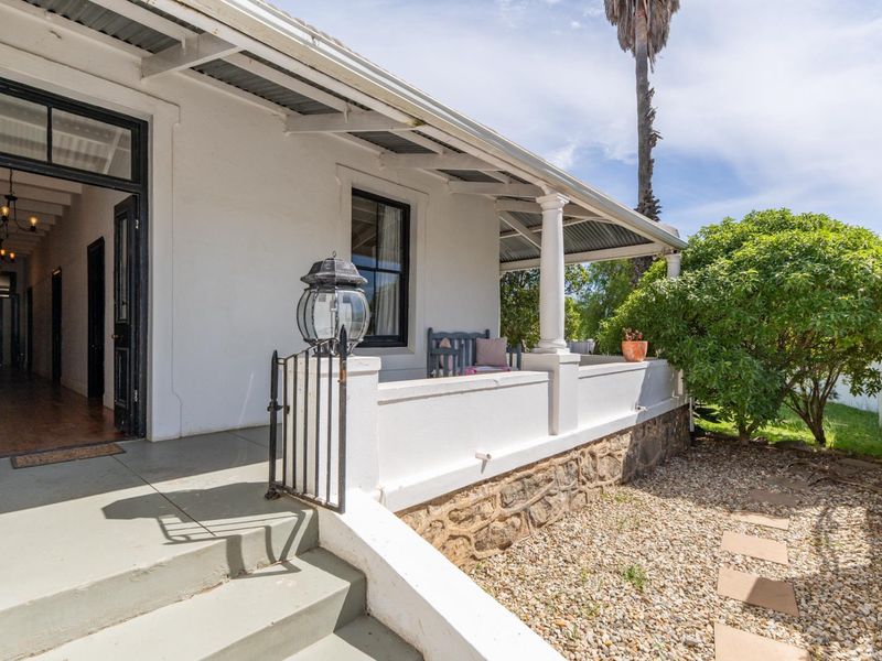 A charming covered veranda featuring classic columns, stone masonry detailing, and direct access to the home's interior through a wide doorway.