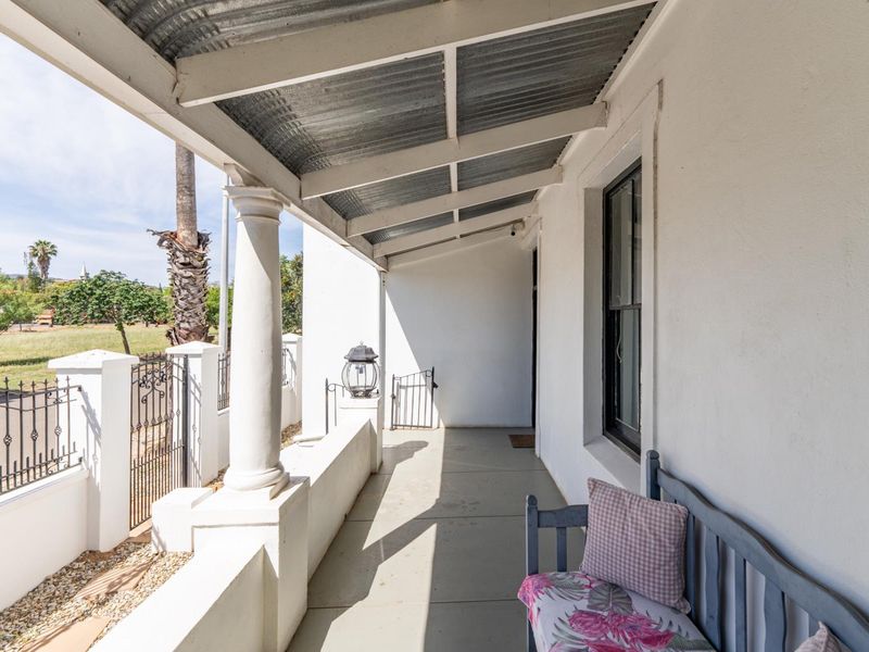 A covered front veranda featuring a corrugated iron roof, classical column support, and wrought iron fencing overlooking the street.