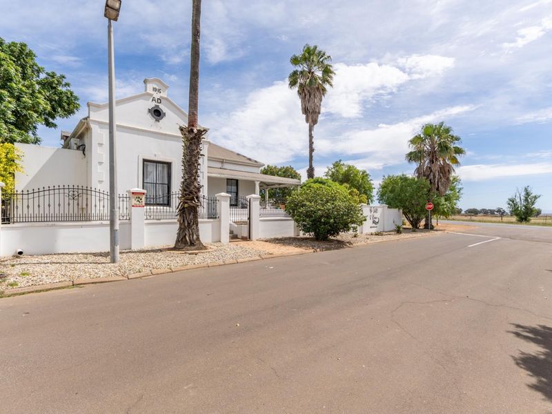 A well-maintained historic house featuring a gabled facade, veranda, and secure perimeter wall, situated on a corner lot with established landscaping.