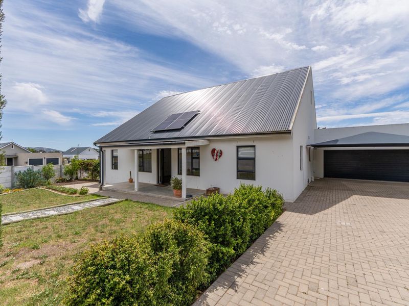 A well-maintained modern house featuring a corrugated metal roof with solar panels, a paved driveway, a garage, and a neat front garden.