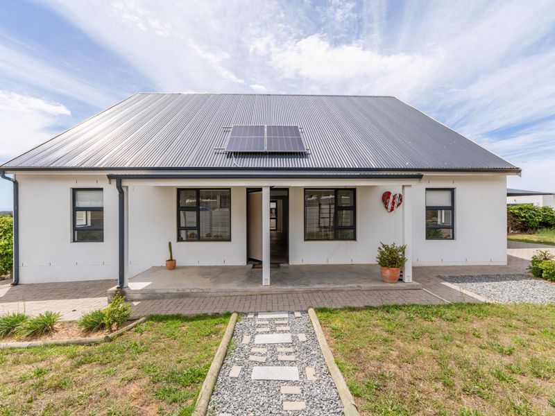 A well-maintained single-story home featuring a corrugated metal roof with integrated solar panels, a covered front porch, and a neat paved entrance walkway.
