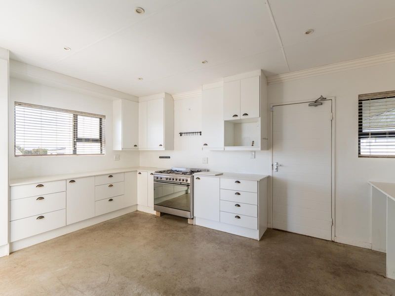 A bright, empty kitchen featuring white cabinetry, a stainless steel gas stove, and concrete flooring, offering a clean canvas for customization.