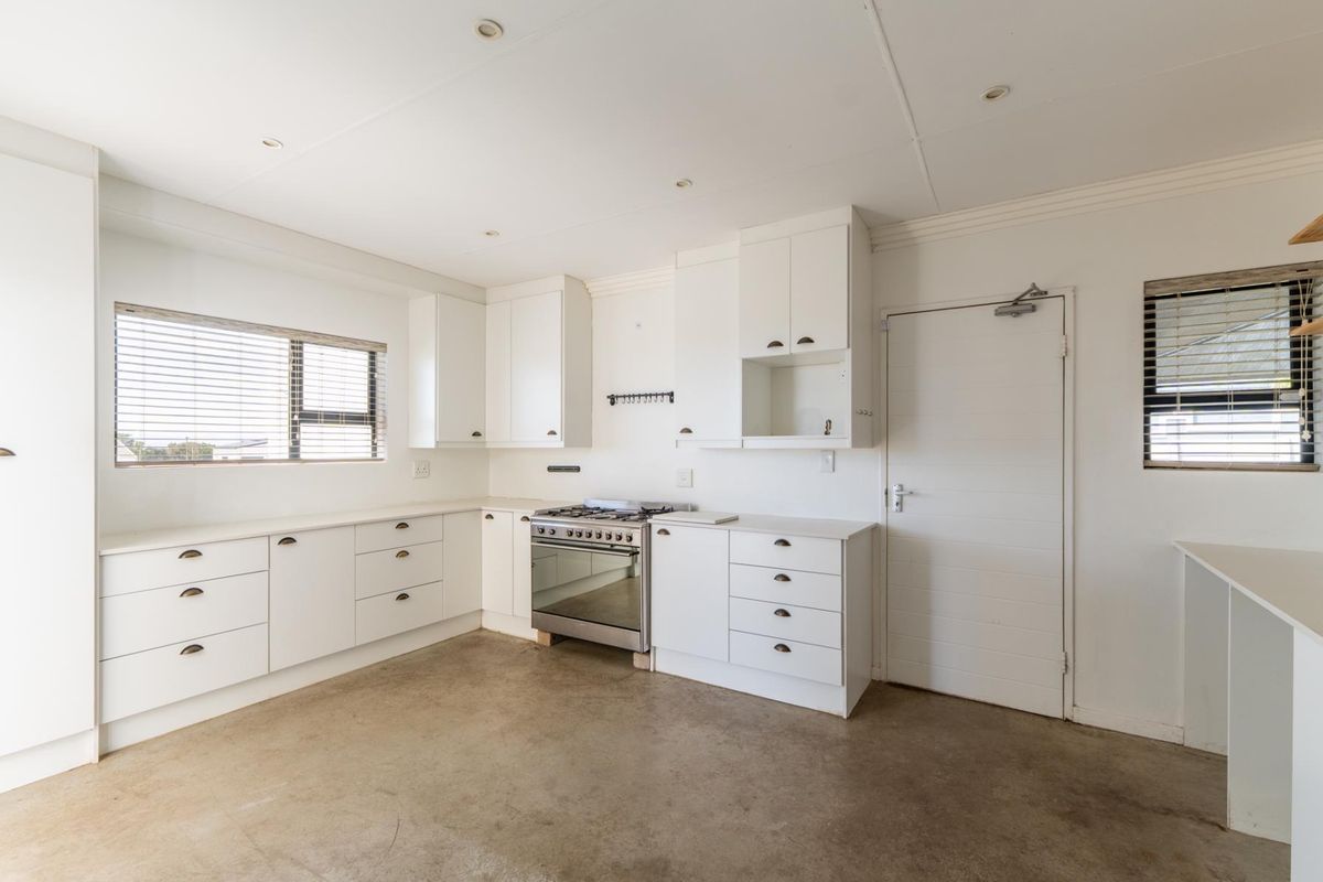 A bright, empty kitchen featuring white cabinetry, a stainless steel gas stove, and concrete flooring, offering a clean canvas for customization.