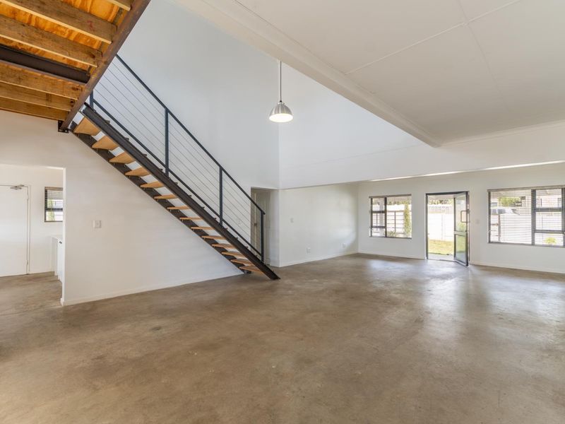 Spacious open-plan living area featuring polished concrete floors, a modern industrial-style staircase, and abundant natural light through large aluminium-framed windows.