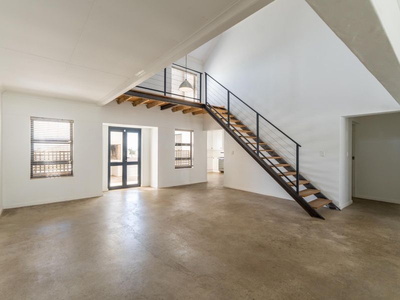 Spacious open-plan living area featuring polished concrete floors, a modern staircase with metal balustrades, and high vaulted ceilings with abundant natural light.