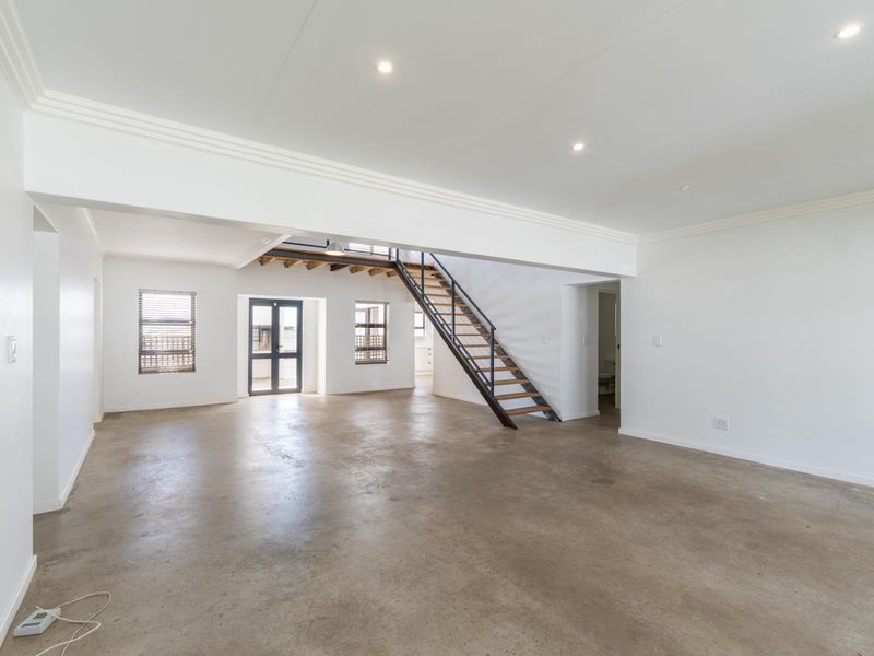 Spacious open-plan living area featuring polished concrete floors, modern staircase, and abundant natural light through aluminium-framed windows.