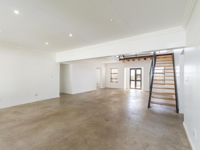 Spacious open-plan living area featuring polished concrete floors, recessed lighting, and a modern staircase leading to an upper level.