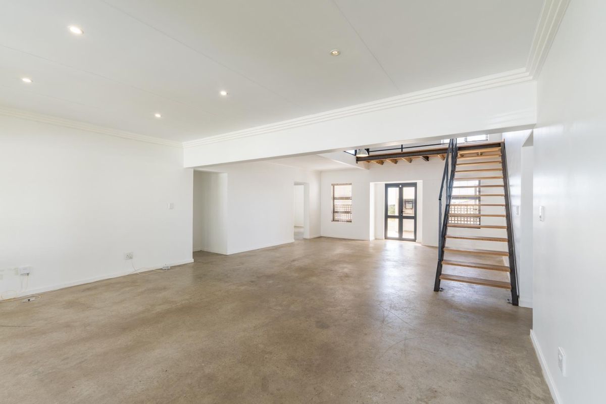 Spacious open-plan living area featuring polished concrete floors, recessed lighting, and a modern staircase leading to an upper level.