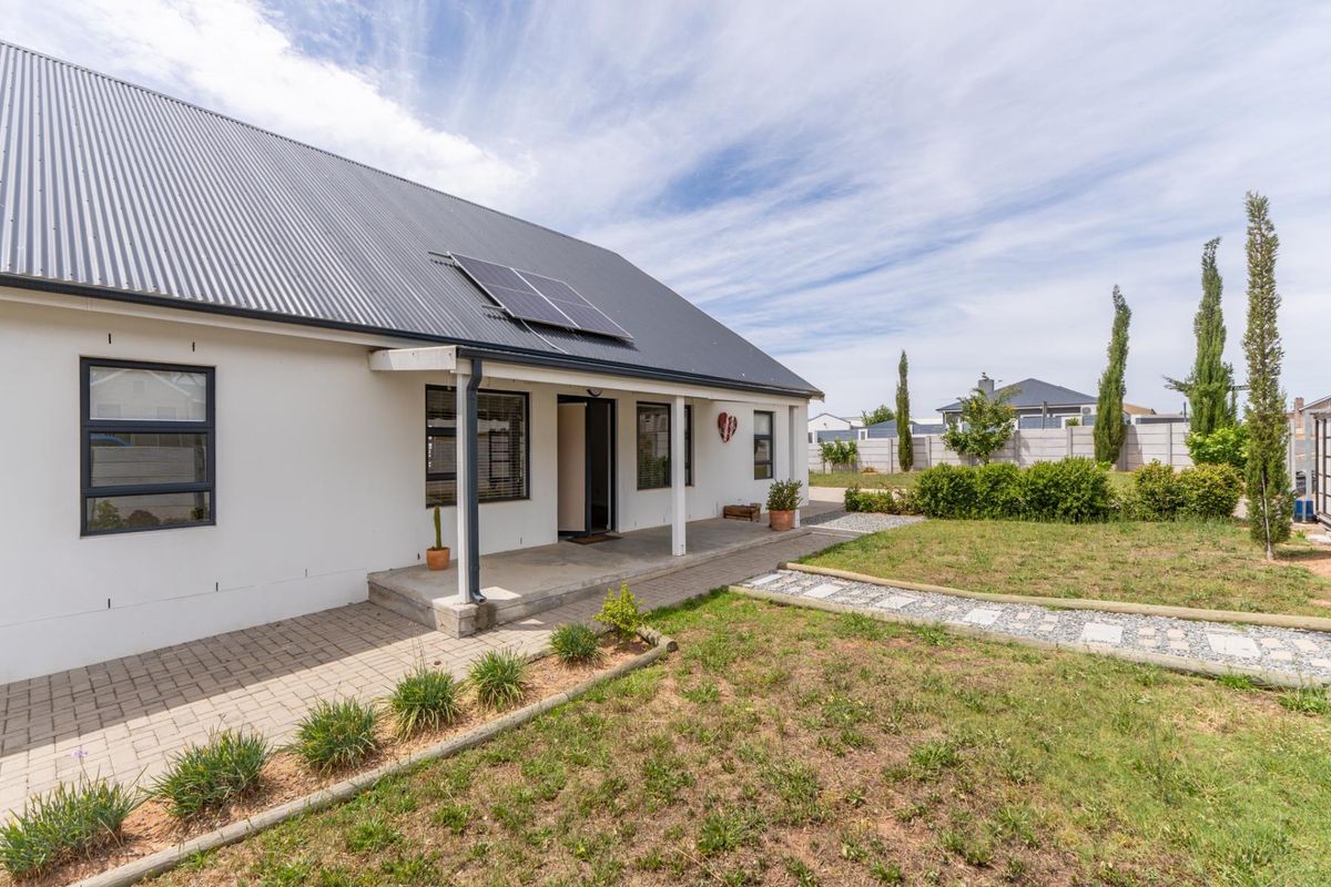 Rear view of the house featuring a covered patio, corrugated metal roof with solar panels, and a landscaped garden with a paved walkway.
