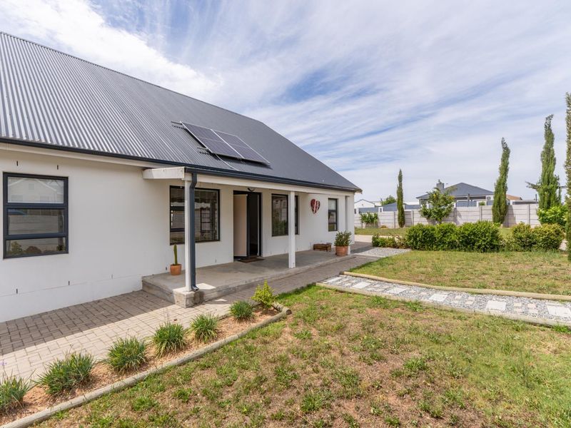 Rear view of the house featuring a covered patio, corrugated metal roof with solar panels, and a landscaped garden with a paved walkway.