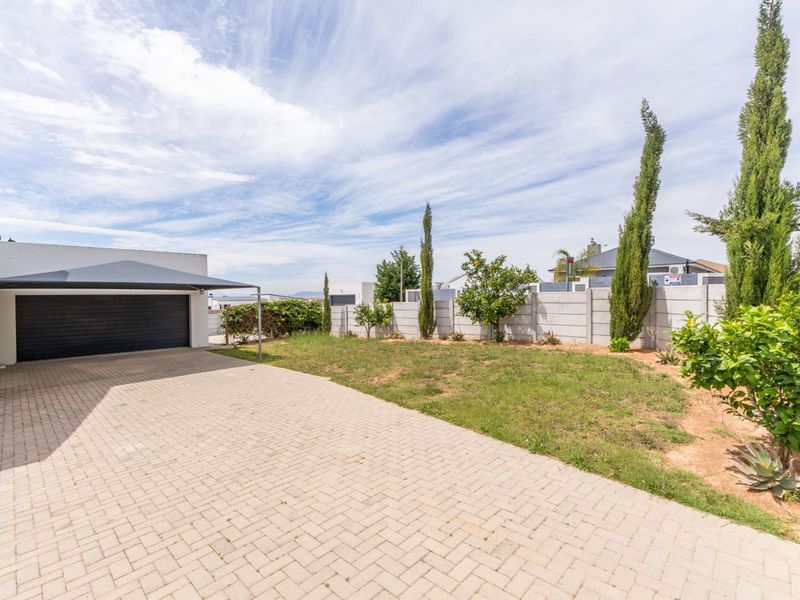 Front exterior view featuring a paved driveway, a covered carport, a garage, and a landscaped garden area with a boundary wall.