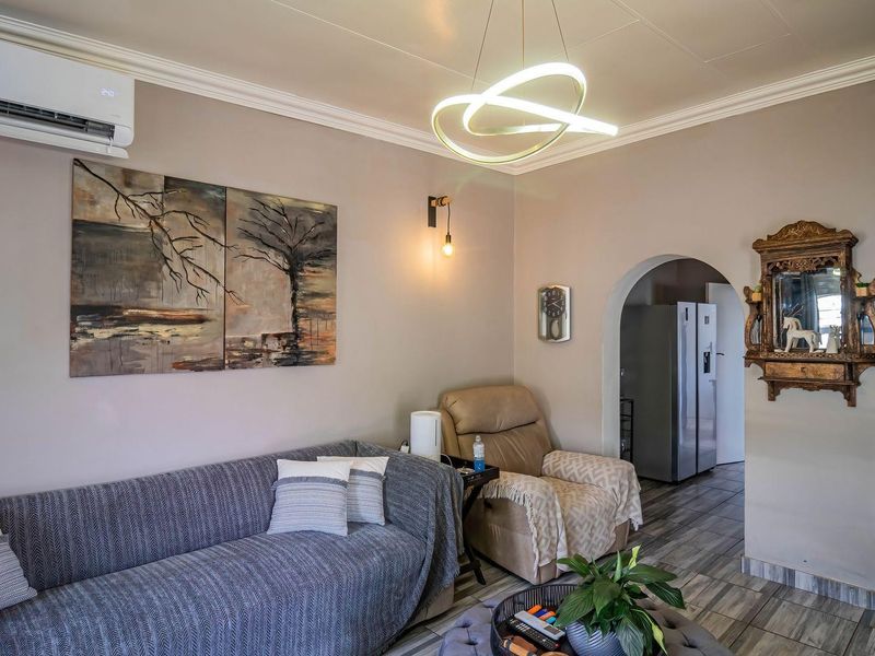 A well-maintained living room featuring tiled flooring, crown molding, and an archway leading to the kitchen area, equipped with a wall-mounted air conditioning unit.