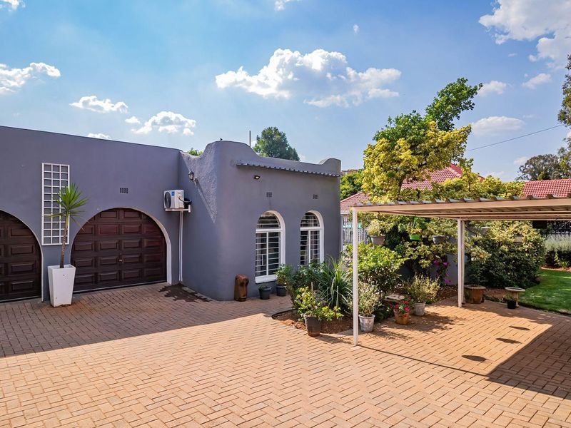 Front exterior view featuring a paved driveway, double garage with arched doors, and a covered carport area.